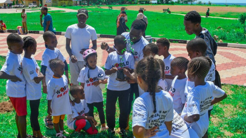 Group of kids and adults wearing world on wheels t shirts planting a tree